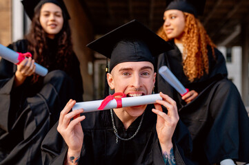 Happy college student biting graduation diploma with friends in background