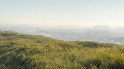 Fototapeta premium Meadow field on the top of a rolling hill with blue sky background of mountain range.Landscape of the countryside,early morning and peaceful landscape.