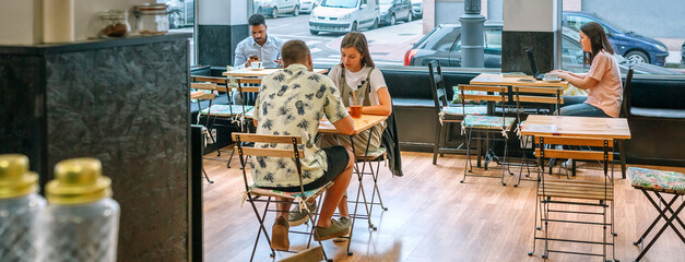 Banner of customers enjoying coffee and working on laptops in a bright, inviting cafe, capturing the essence of modern cafe culture and urban lifestyle in a lively and social atmosphere