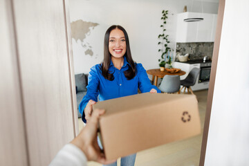 Happy lady customer receiving parcel box from courier hands, standing at door and smiling, thanking...