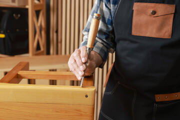 Relaxing hobby. Senior man repairing wooden stool with chisel in workshop, closeup