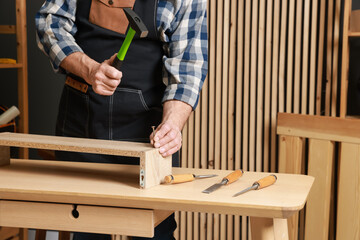 Relaxing hobby. Senior man repairing wooden shelf with hammer and nail in workshop, closeup