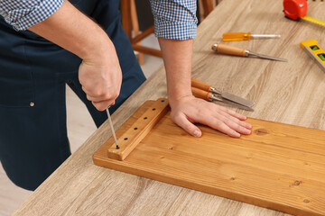 Relaxing hobby. Man working with wooden plank and screwdriver at table indoors, closeup