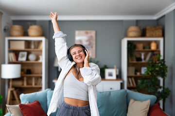Happy young beautiful cheerful woman listening to music through wireless headphones and dancing at...