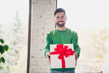 Man in green sweater holding a gift box with red bow, expressing joy indoors
