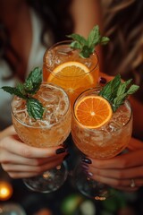 Three girls hold cocktails garnished with orange and mint