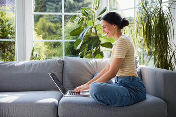 Young woman using laptop while sitting on sofa at home