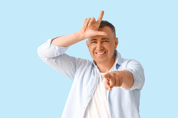 Mature man showing loser gesture on blue background