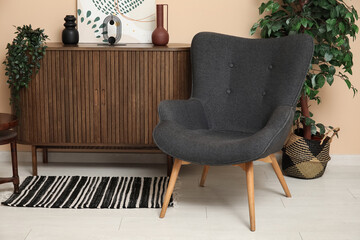 Dark grey armchair with dresser, houseplants and rug near beige wall
