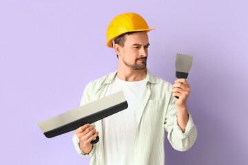Male decorator with putty knives on lilac background