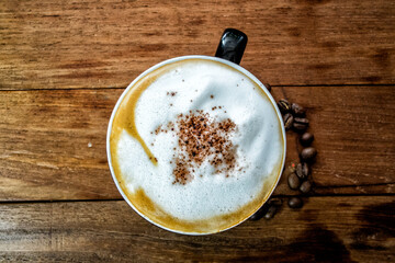 Top-down view of a cappuccino in a dark cup on a wooden table. Frothy milk with spice sprinkles....