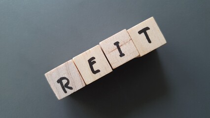 REIT acronym made of wooden letter cubes on dark background. Real Estate Investment Trust