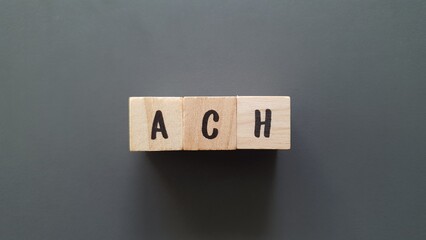 ACH acronym made of wooden letter cubes on dark background. Automated Clearing House