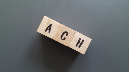 ACH acronym made of wooden letter cubes on dark background. Automated Clearing House