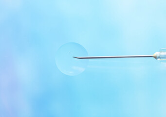 Close-up of an injection needle with a drop of transparent liquid at the end, on a light blue blurred background. Macro photo, soft light, blur effect. Copy space