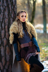 Beautiful blonde girl with hairstyle in fur medieval dress  posing in  winter sunny forest. Fairy...
