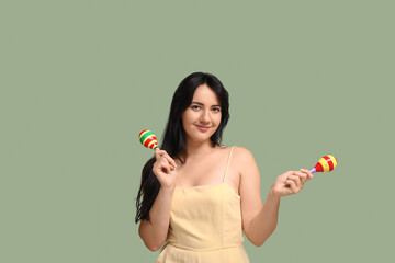 Beautiful happy young woman with maracas on green background
