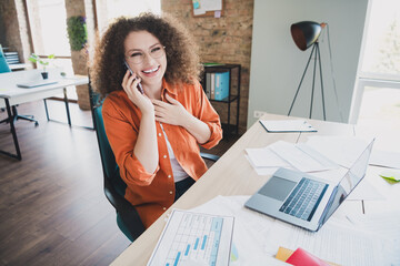 Young professional woman with curly hair talking on the phone in a bright modern office while...