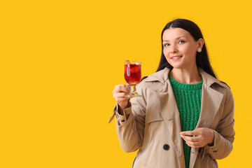 Young woman with glass of mulled wine on yellow background