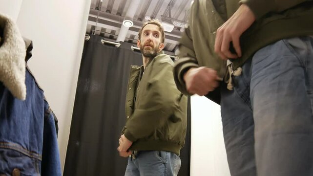 A man trying on a khaki jacket in a fitting room