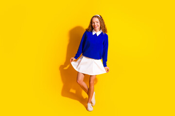 Charming young woman in vibrant blue outfit posing joyfully against a bold yellow background,...