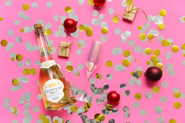 Bottle of champagne with glass and Christmas balls on pink background