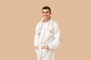 Portrait of handsome young man in bathrobe and towel on beige background
