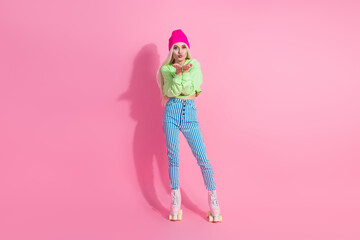 Young stylish woman in colorful outfit posing on pink background, expressing playful gestures,...