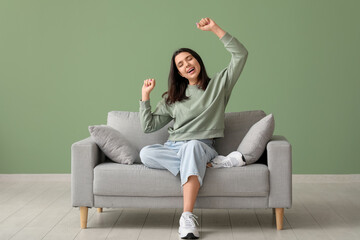 Beautiful young happy woman sitting on comfortable sofa near green wall