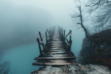 Mysterious wooden bridge shrouded in dense fog over a calm, turquoise river, creating an eerie, tranquil atmosphere amid bare trees in a misty, surreal landscape.