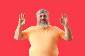 Mature bearded man showing OK on red background