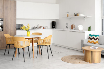 Interior of light modern kitchen studio with dining table, armchairs, mimosa flowers, counters and sofa