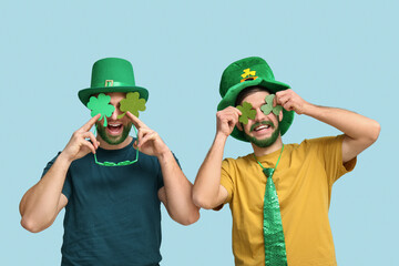 Young men in leprechaun hats with green beards holding clover on blue background. St. Patrick's Day...