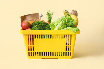 Yellow shopping basket full of different fresh products and apples on beige background