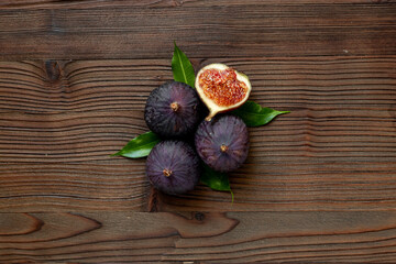 Fresh ripe figs whole and cut with green leaves on wooden table. Top view
