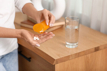Woman with medicines and glass of water at home. Closeup