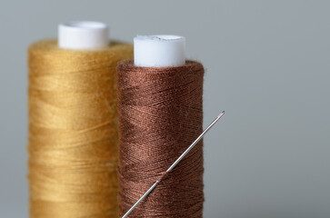 Brown and bronze thread spools with needle on gray background with copy space for text close-up