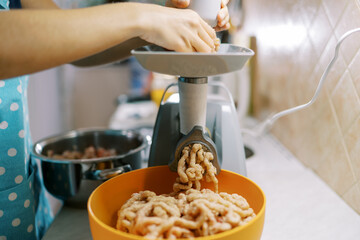 Cook twists minced meat on an electric meat grinder into a bowl on the table
