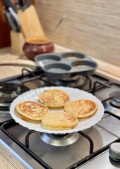 Delicious pancakes are prepared on a modern and stylish stove in a circle pan in the equipped kitchen. Delicious pancakes with fresh vegetables are being expertly prepared on an elegant kitchen stove