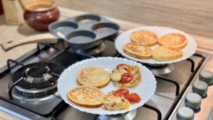 Delicious pancakes are prepared on a modern and stylish stove in a circle pan in the equipped kitchen. Delicious pancakes with fresh vegetables are being expertly prepared on an elegant kitchen stove