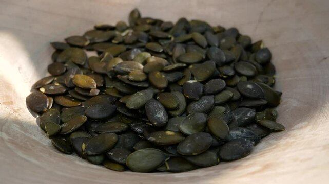 Pumpkin seeds are poured into a wooden plate. Pumpkin seeds as a nutritious superfood. Healthy snack. A source of nutrients in a healthy diet.