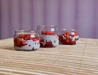 A lot of healthy Chia pudding with coconut milk in a glass containers in view can with fresh berries as raspberry, red currant, cranberry and pieces of peach on bamboo background. Close-up