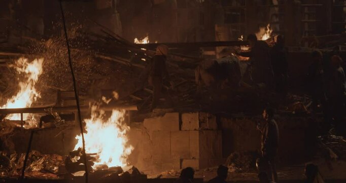 Varanasi, Uttar Pradesh, India. Cremation in process on Manikarnika Ghat. Cinematic Camera movement moving along riverbank embankment. View from riverside. night lights. Fire, smoke - Funeral rites of