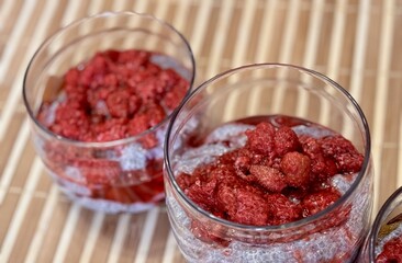 A lot of healthy Chia pudding with coconut milk in a glass containers in view can with fresh berries as raspberry, red currant, cranberry and pieces of peach on bamboo background. Close-up