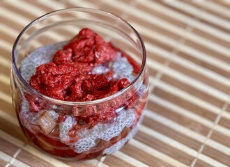 Healthy Chia pudding with coconut milk in glass container in view can with fresh berries as raspberry, red currant, cranberry and pieces of peach on bamboo background on store counter. Close-up
