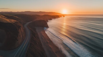 Fototapeta premium An aerial shot of a stunning coastal road with sweeping ocean views, dramatic cliffs, and the sun setting on the horizon, casting a golden glow.
