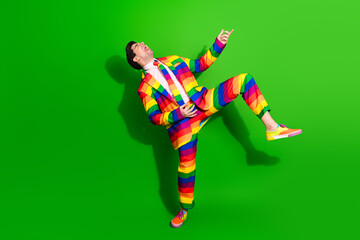 Young man in a colorful rainbow suit joyfully posing against a vibrant green background, expressing...