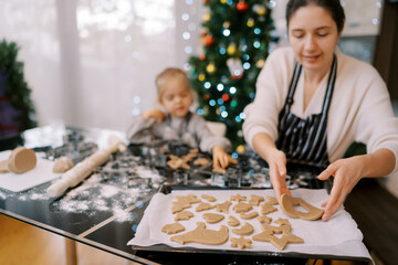 Mom puts cut out cookies on a baking sheet while sitting at the table with her little girl