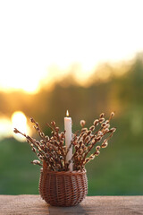 Burning candle and willow branches in basket outdoor, abstract nature background. Easter holiday,...