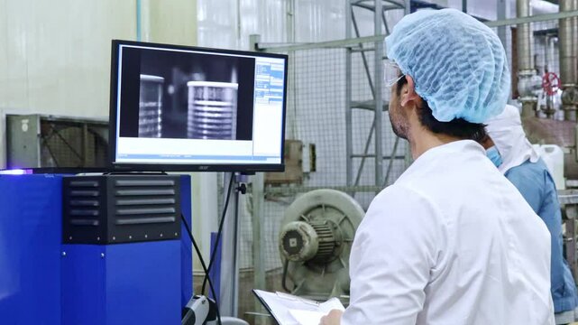Male QC worker looks at the screen controlling the metal detector scanner X-ray machine canned fish on the production line contaminants in canned food before packing into boxes in the packing room.